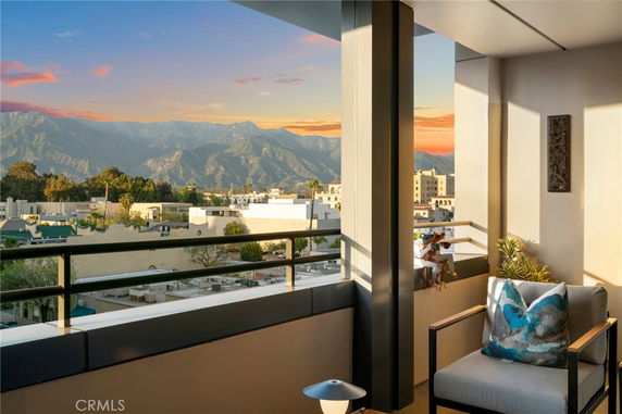 Panoramic view from a building balcony showing mountains and cityscape at sunset.