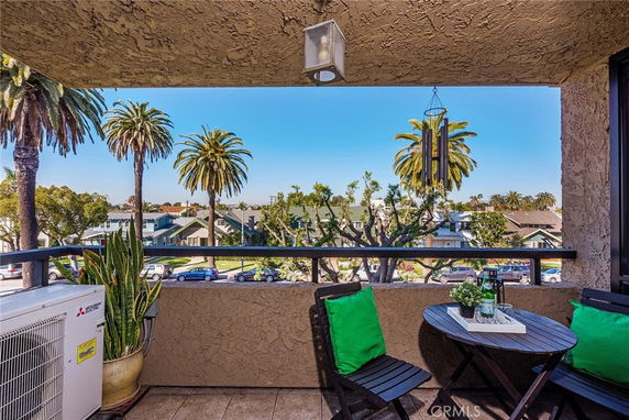 Balcony with a table and chairs overlooking palm trees and houses.