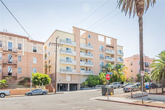 Front view of a multi-story apartment building with balconies and a parking area in an urban setting.