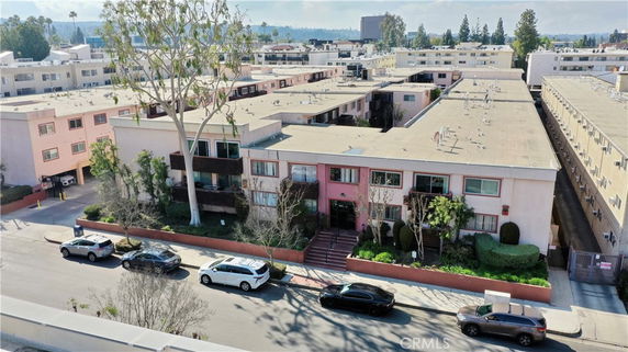 Front view of a multi-story apartment building with several cars parked on the street.