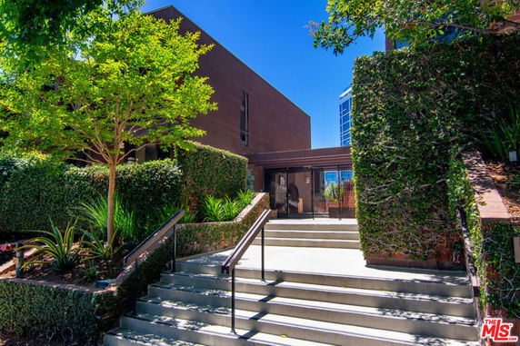 Front view of a modern building with a staircase and greenery.