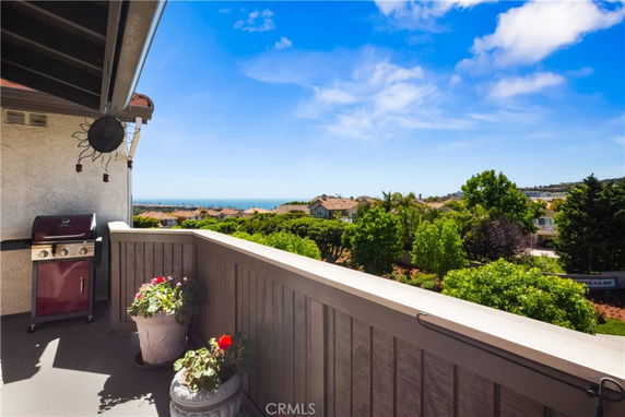 Balcony view overlooking residential area with trees and distant ocean.