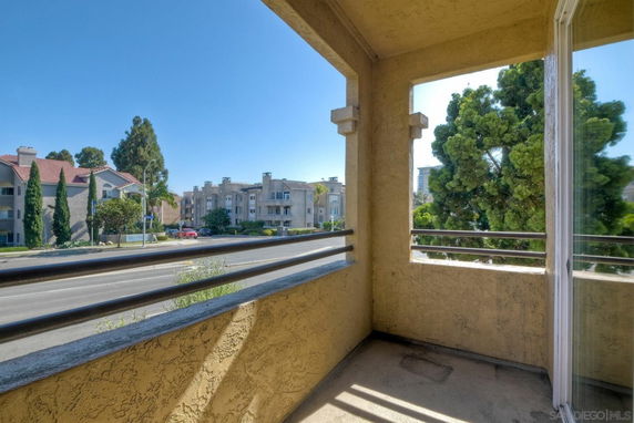 Balcony view from a building showing adjacent residential structures and trees.