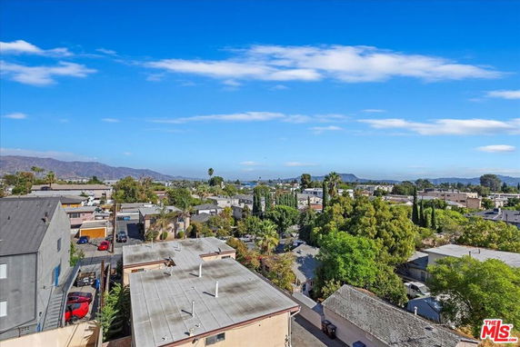 Panoramic view of a suburban area with buildings, trees, and distant mountains under a blue sky.