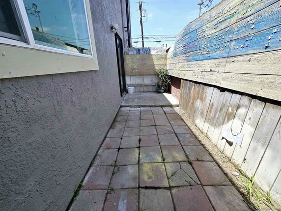 Narrow outdoor walkway with brick paving and decorated wooden fence.