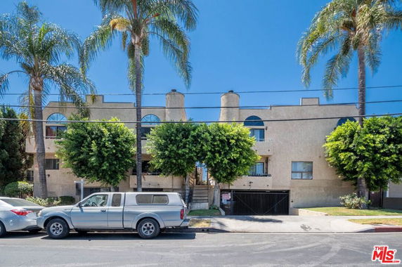 Front view of a multi-story residential building with arched windows and a gated parking area.