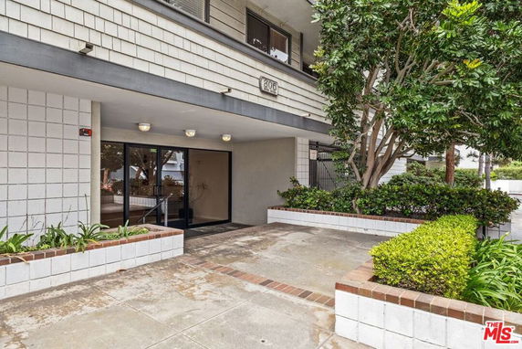Entrance view of a building with a glass door and canopy, surrounded by shrubs and trees.