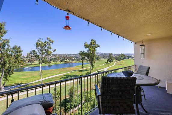 Balcony view over a golf course with a lake and trees in the background.