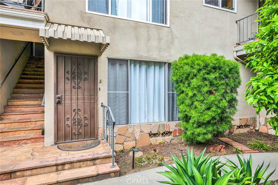 View of the entrance to a residential building with a metal door and surrounding plants.