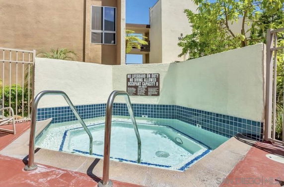 Outdoor jacuzzi area with blue-tiled steps and surrounding wall, near a building.