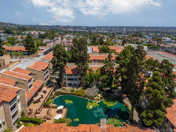 Aerial view of a residential complex with red-tiled roofs surrounded by greenery and a central pond.