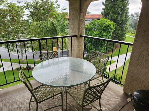 Balcony view with a glass table and chairs overlooking greenery and pathways.