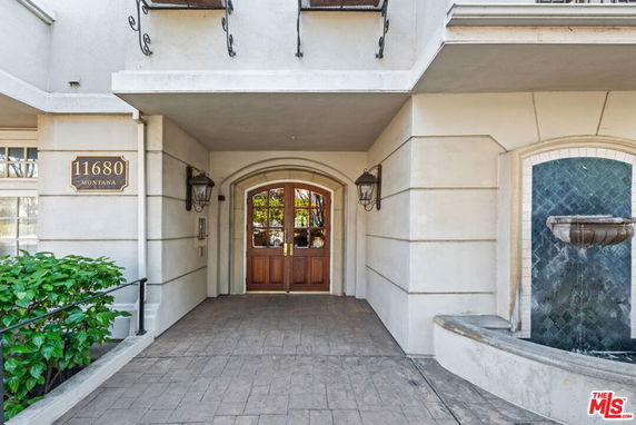 Front view of a building entrance with a wooden door and a wall-mounted fountain.