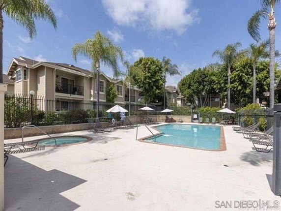 Outdoor swimming pool area with lounge chairs and parasols near apartment buildings.