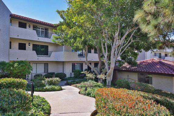 Front view of a multi-story residential building with balconies and landscaped surroundings.