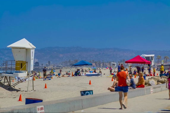 Beach scene with lifeguard tower and people under tents.