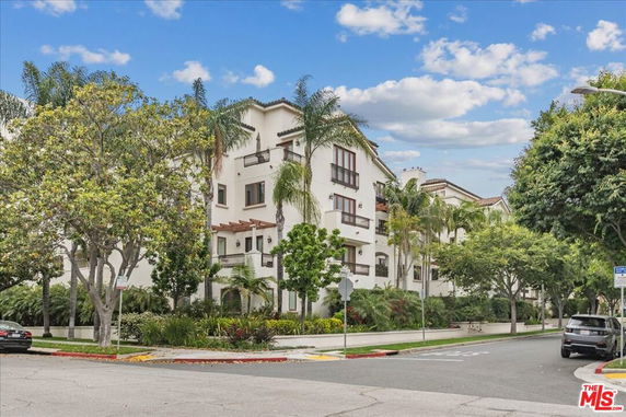 Front view of a multi-story residential building with balconies and surrounding trees.