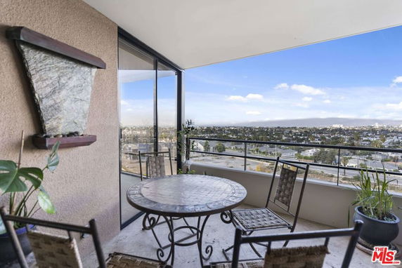 Balcony with a round table and chairs overlooking a cityscape.