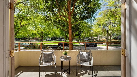 Balcony view with two chairs and a table overlooking a street lined with trees.