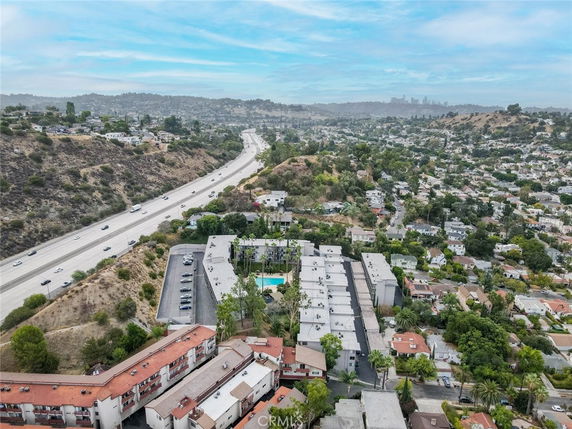 Aerial view of a residential area with houses and a highway visible, set against a backdrop of hills and distant cityscape.