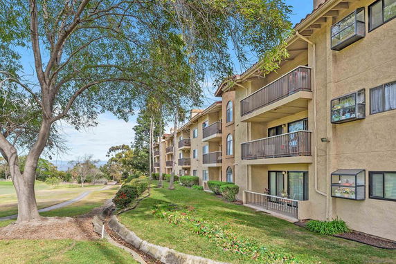 View of a multi-story apartment building with balconies surrounded by trees and grassy areas.