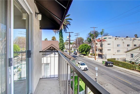 View from a building balcony overlooking a street with nearby residential buildings.