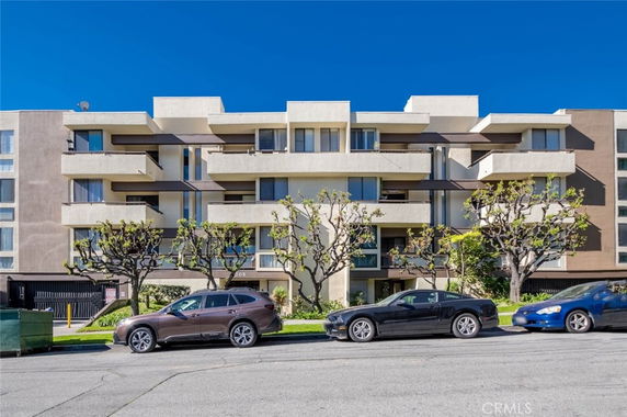 Front view of a multi-story apartment building with balconies and parked cars in front