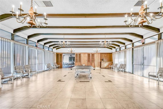 Interior view of a recreational area with a ping pong table and seating, featuring chandeliers and beamed ceilings.