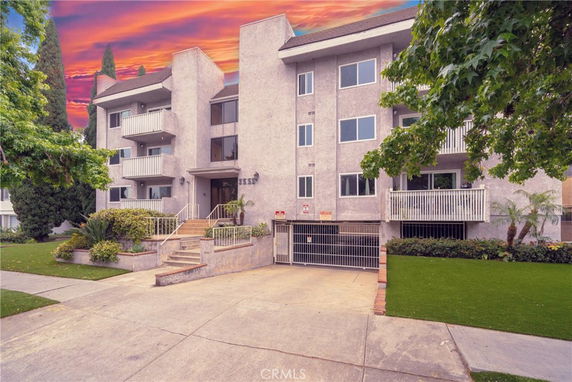 Front view of a multi-story apartment building with balconies and a gated parking area.