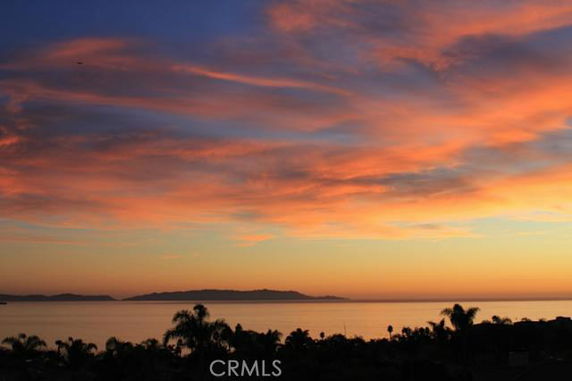 Panoramic view of the ocean and distant land at sunset with colorful sky.
