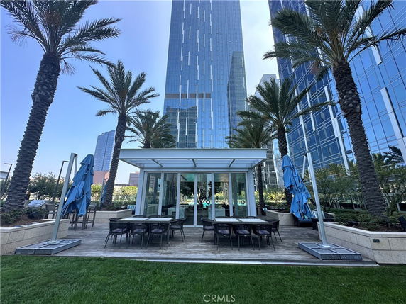 View of a modern high-rise building surrounded by palm trees with an outdoor seating area in the foreground.