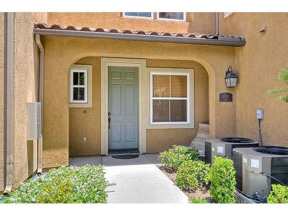 Front view of a house entrance with a green door and window, featuring exterior lighting and air conditioning units.