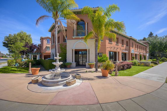 Front view of a two-story building with a fountain and palm trees.