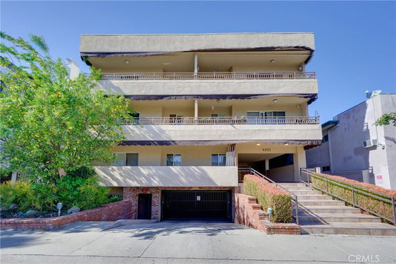 Front view of a multi-story residential building with balconies and a parking area at the ground level.