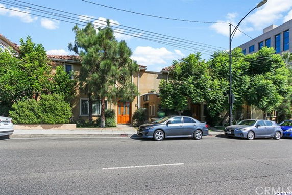 Front view of multi-story building with trees and cars parked in front.