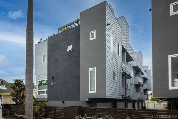 Side view of a modern multi-story building with a gray facade and multiple balconies.