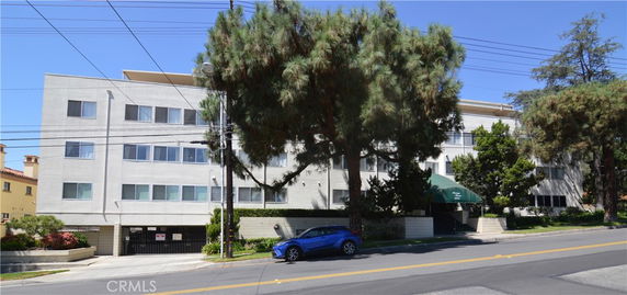 Front view of a multi-story apartment building with trees and a driveway.