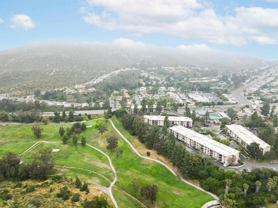 Aerial view of residential buildings surrounded by greenery with hills in the background.