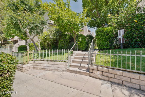 Front view of a building with steps leading to the entrance and surrounded by greenery and trees.