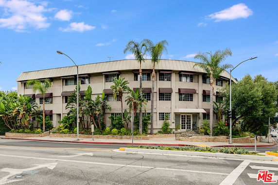 Front view of a multi-story building with vegetation and palm trees.