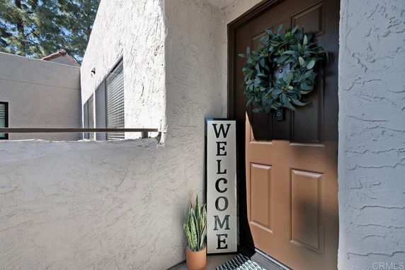 Front view of a house entrance with a brown door, welcome sign, and decorative plant.