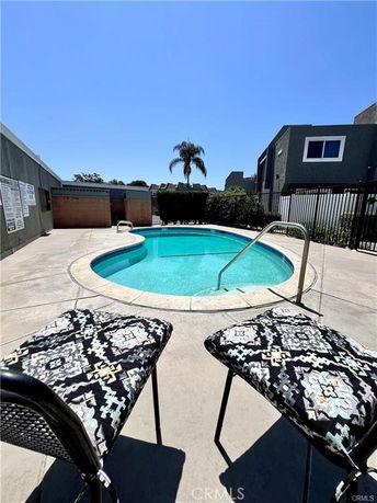 Outdoor swimming pool with surrounding concrete patio and two chairs.