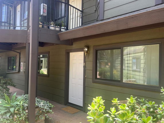 Front elevation view of a two-story apartment building with balconies and potted plants.