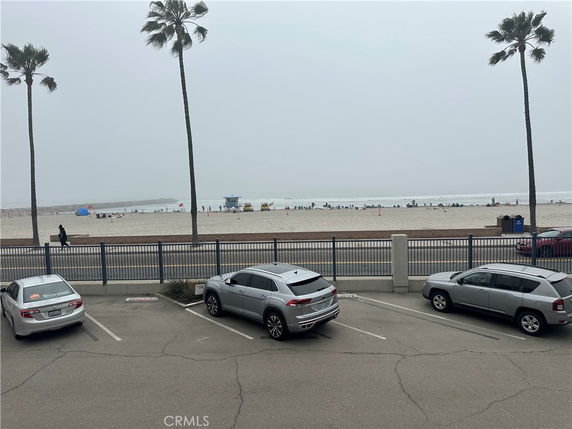 View of parking area near a beach with palm trees and ocean in the background.