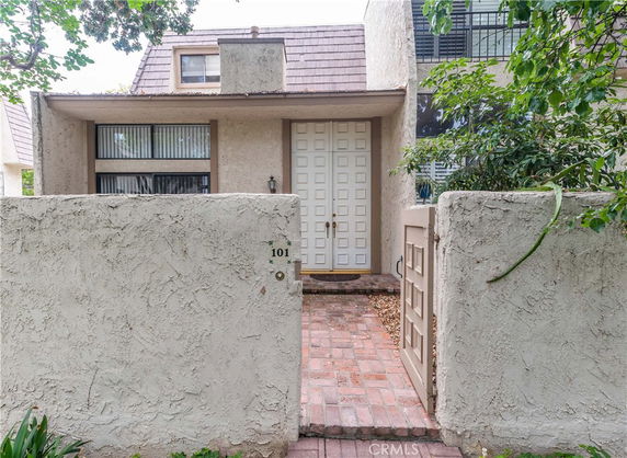 Front view of a house with textured walls and a double door entry, featuring a brick pathway and small gate.
