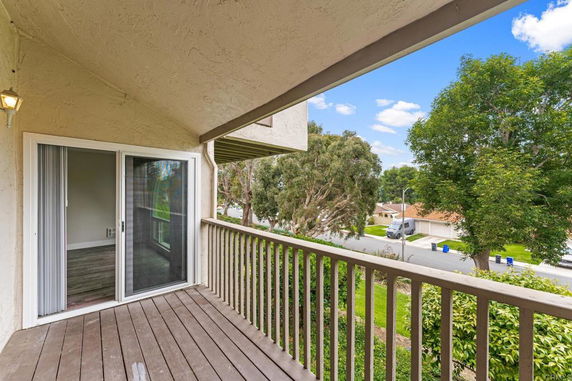 Balcony with railing overlooking a street with trees and houses.
