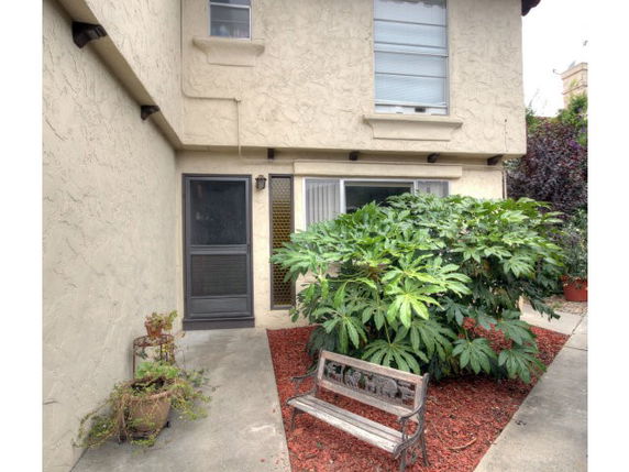 Front view of a two-story building with a small courtyard featuring a bench and plants.