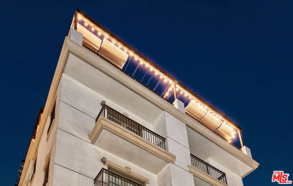 Front view of a multi-story building with balconies and lights on the rooftop.