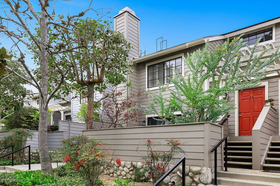 Front view of a two-story house with a red door and surrounding greenery.