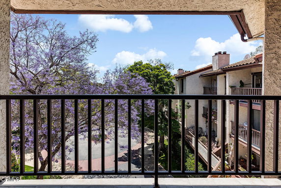 View of surrounding apartment buildings from a balcony with purple flowering trees and a clear sky.